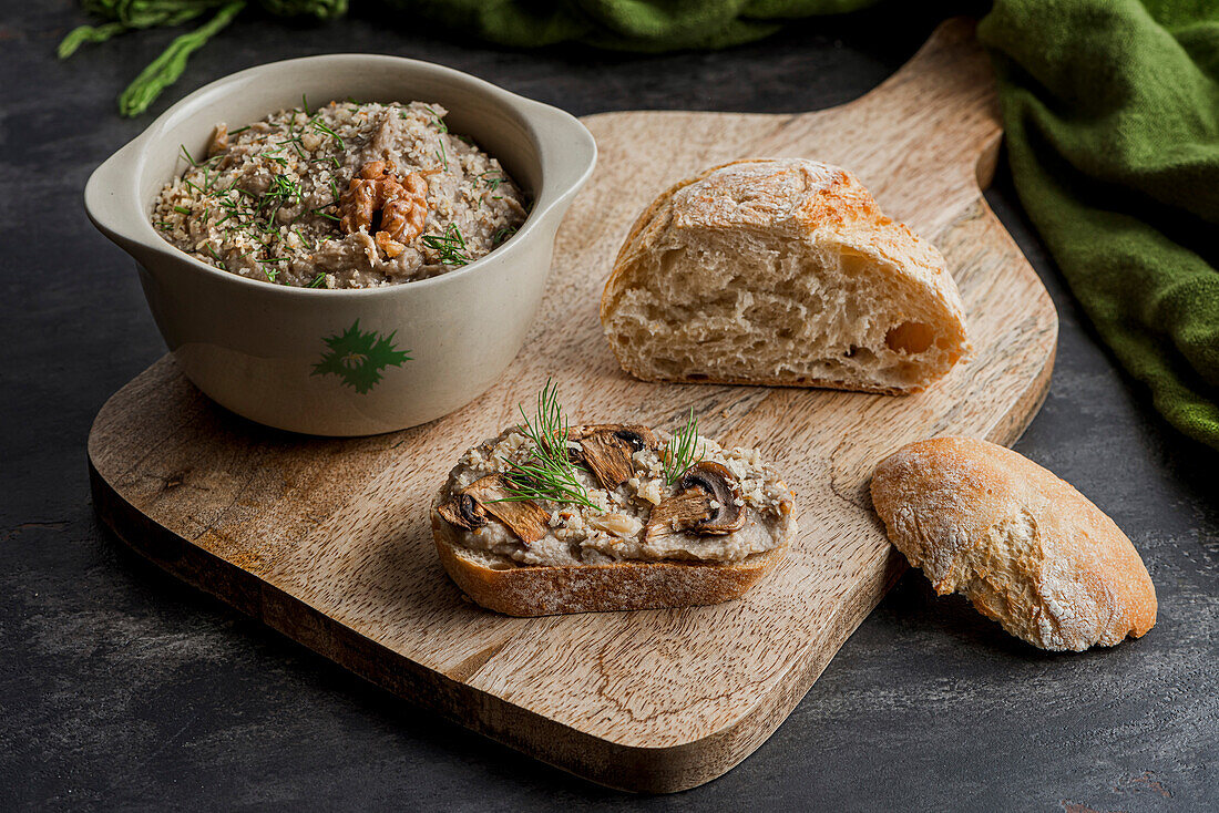 The bowl of mushroom pate, a sandwich and a side of bread on a cutting board.
