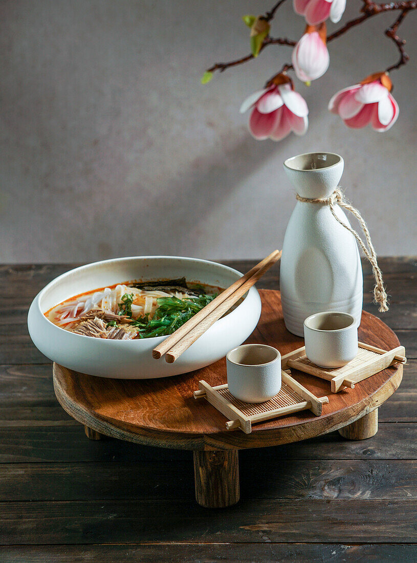 Japanische Sake-Komposition mit asiatischer Suppe mit Reisnudeln, asiatische Essenszeremonie mit Magnolienblüten