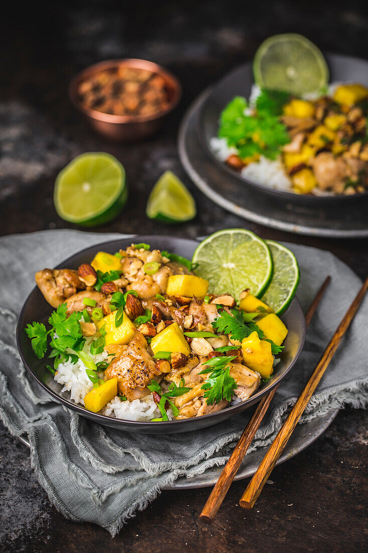 Chicken and Mango stir fry with sliced lime and coriander, in dark bowls with rice and chopsticks