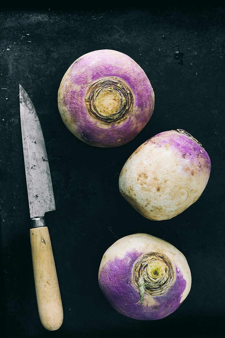 Three purple and white raw beetroot with a knife on a black background