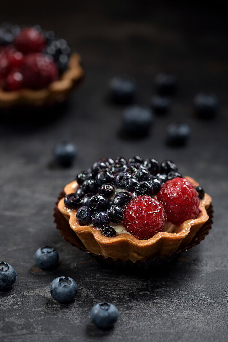 Pastry basket with blueberries and raspberries. Cake on a dark background