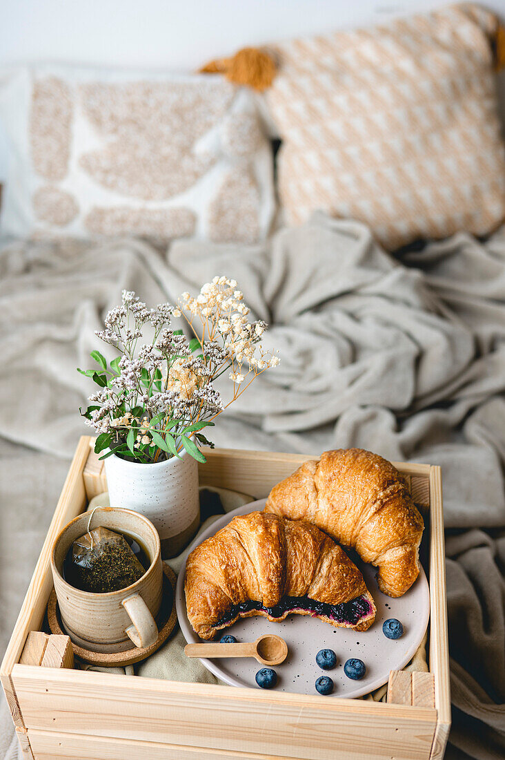 Frühstück im Bett mit frisch gebackenen Croissants mit Blaubeermarmelade und Tee in einem Becher