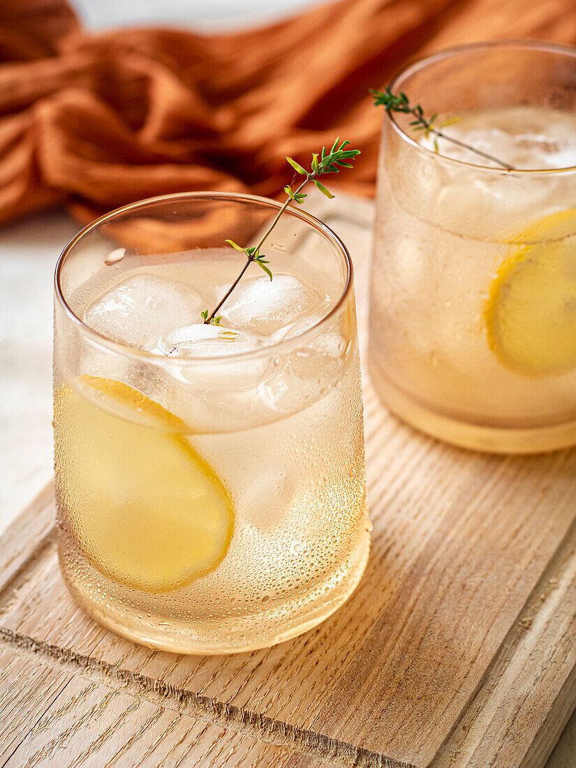 Glass of water with ice cubes decorated with a lemon slice and thyme