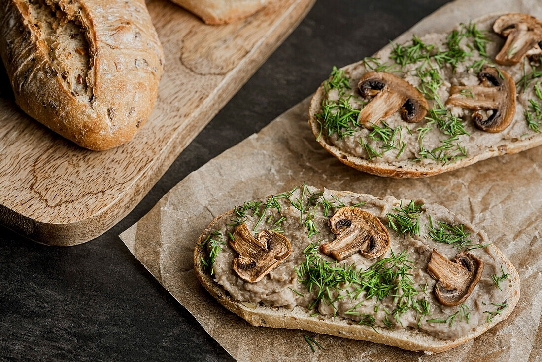 Sandwiches mit Pilzpastete und Champignons auf Kraftpapier. Brot auf einem Schneidebrett