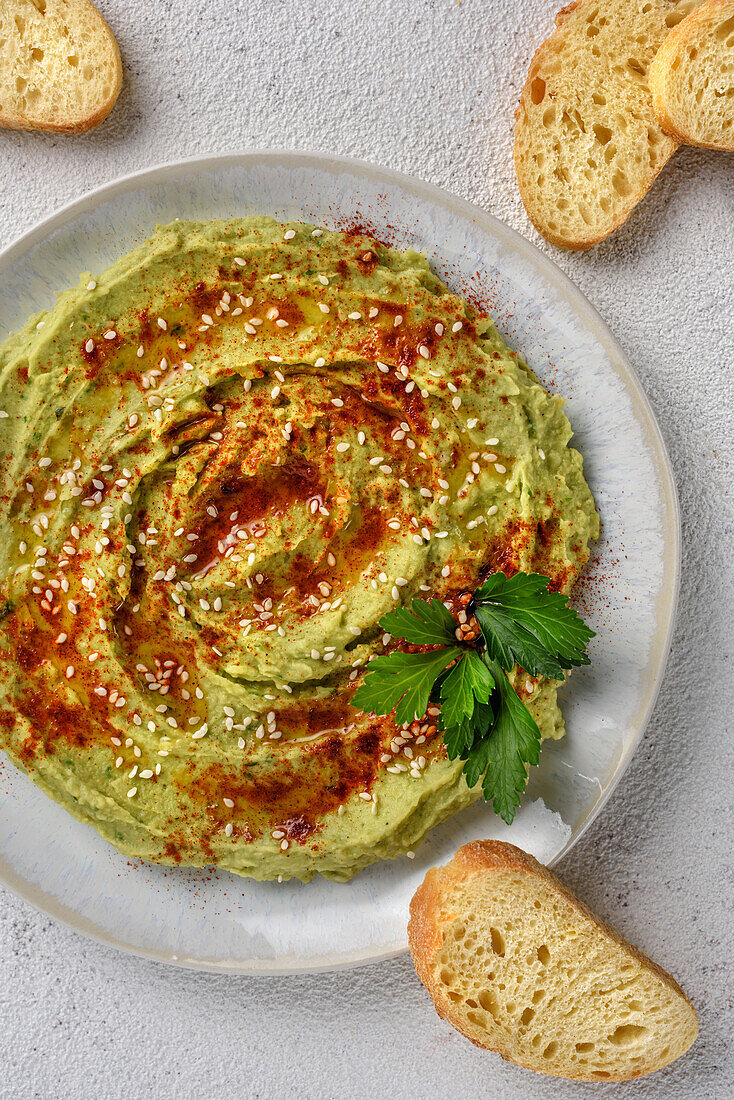 Avocado hummus flavoured with sesame seeds, paprika and parsley. The dish is served with toast