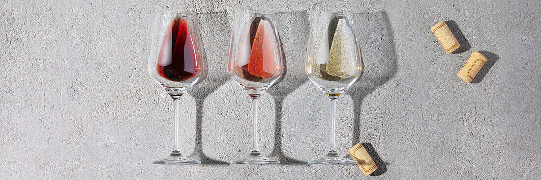 Weinkomposition mit Rot-, Rosé- und Weißwein in Gläsern, schönes Sonnenlicht und Schatten auf grauem Hintergrund. Draufsicht, flach gelegt. Weinbar, Weingut, Weindegustation Konzept. Minimalistische trendige Fotografie