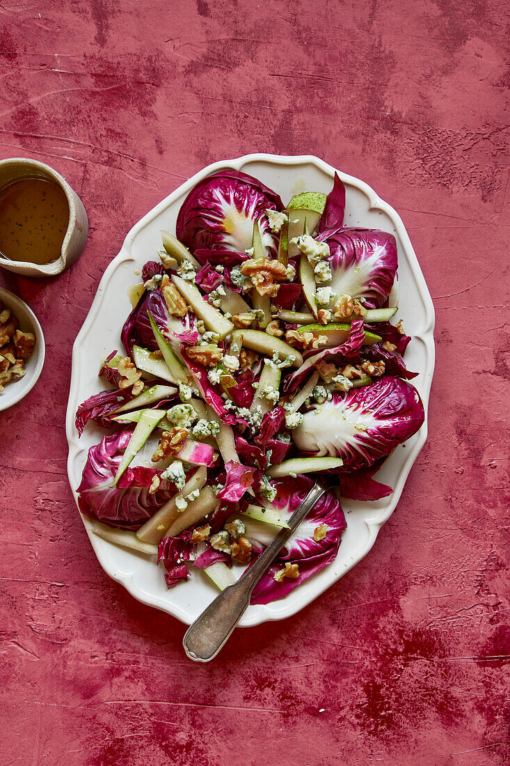 Raddichio-pear-walnut-blue cheese salad on a white oval plate on a pink background, with dressing