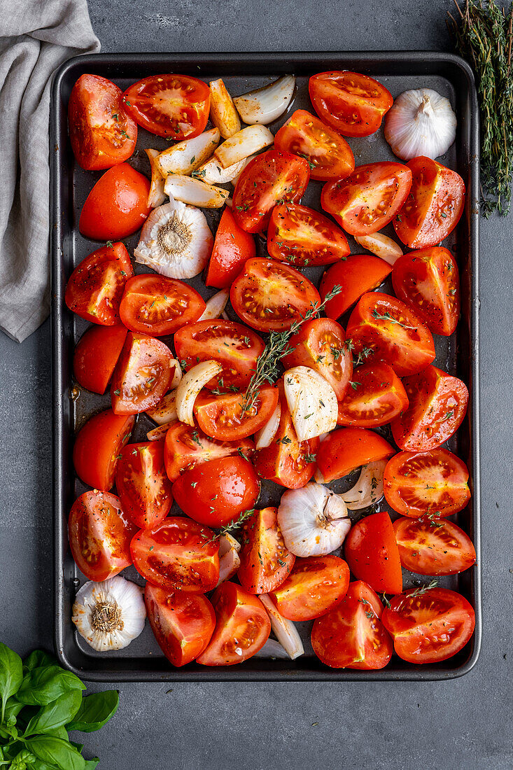 Tomato slices, onion slices and garlic halves on a baking sheet to be roasted.