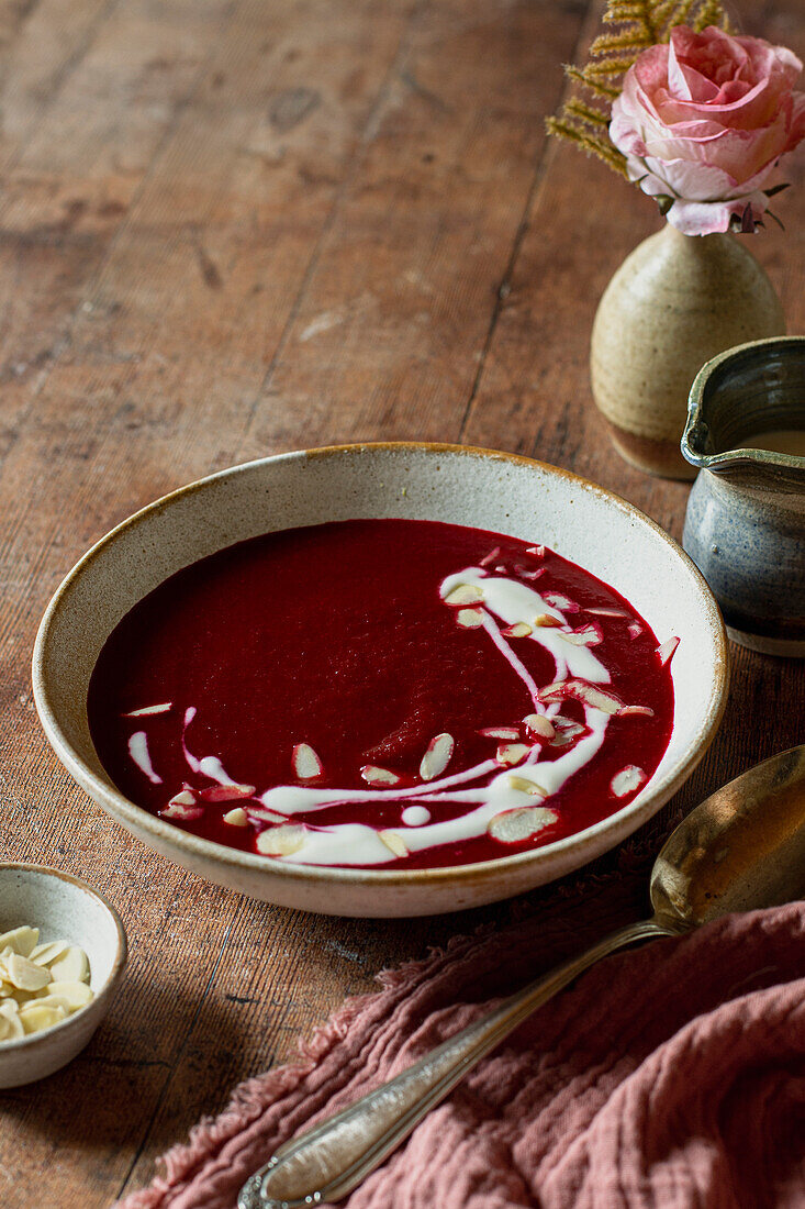 A bowl of beetroot soup with cream and flaked almonds on a wooden table