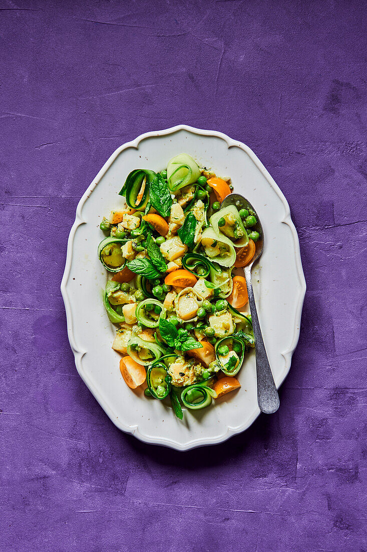 Green pea, cucumber, potato and tomato salad on a purple background