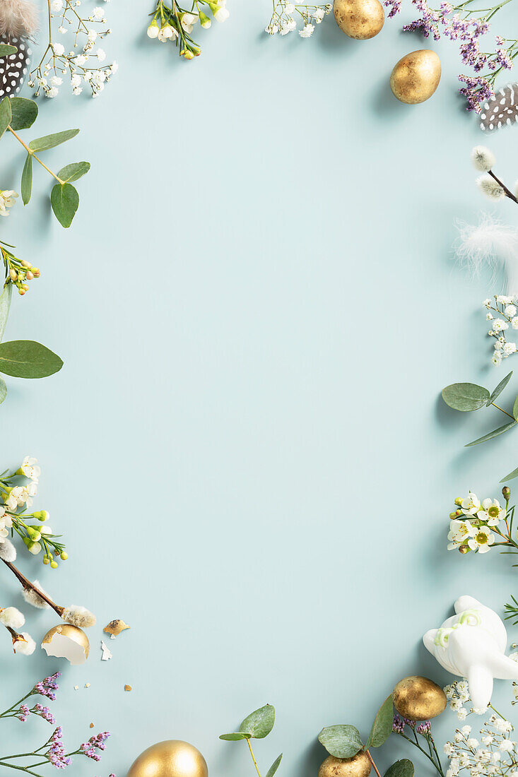 Easter table decoration. Happy Easter concept with golden Easter eggs, feathers and spring flowers on blue background. Flat lay top view copy space