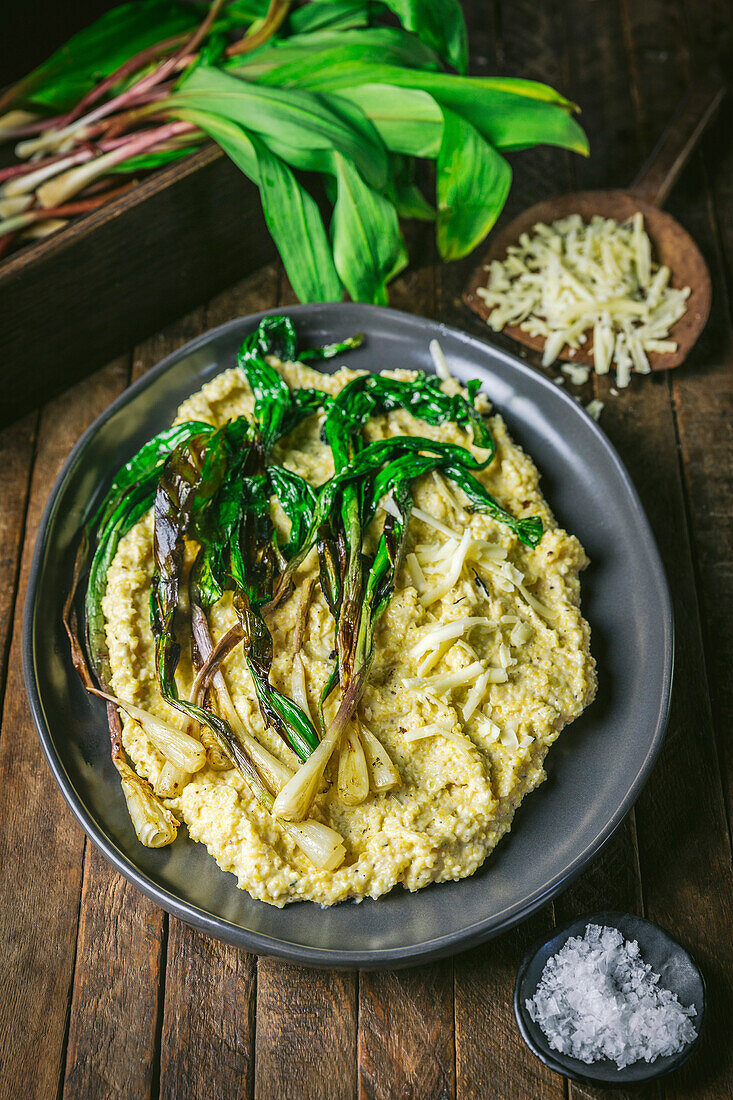 Polenta and grilled ramps on a platter with fresh ramps and grated cheese in background