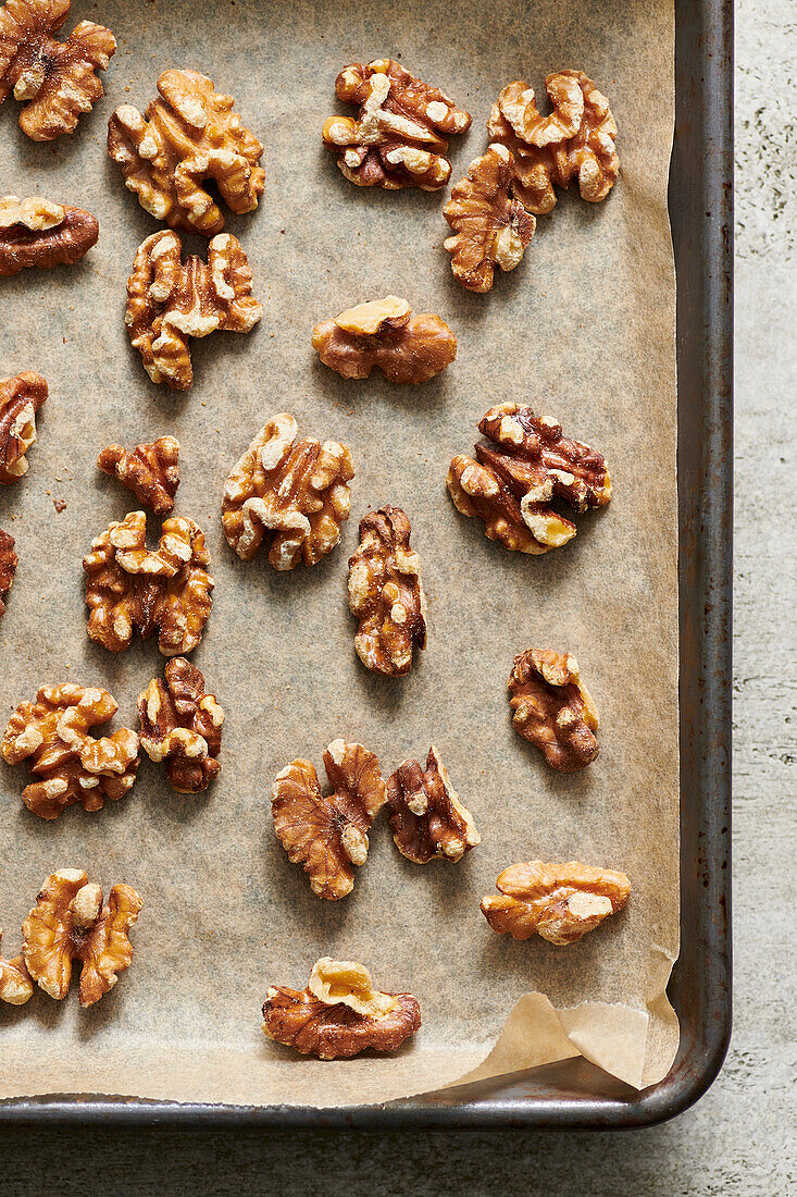 Toasted walnuts on parchment paper on a sheet pan.