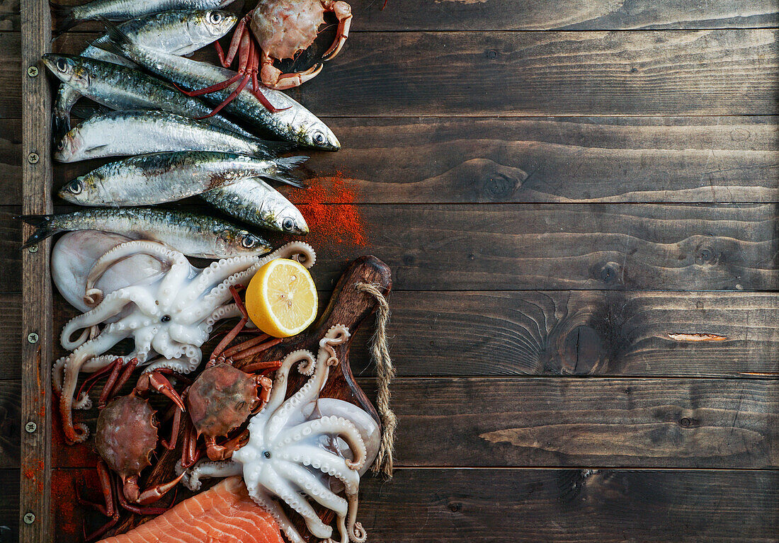 Meeresfrüchte-Tafel mit Krabben, Sardinen und Muscheln, Fisch und Tintenfisch auf dunklem Holzuntergrund. Draufsicht, Nahaufnahme
