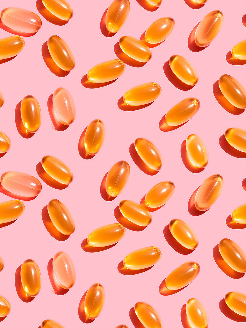 Composition of orange-coloured vitamin pills on a pink background in a bright studio, top view
