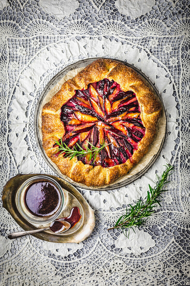 Rustic Plum Galette with red wine caramel sauce and a fresh rosemary sprig on intricate lace background