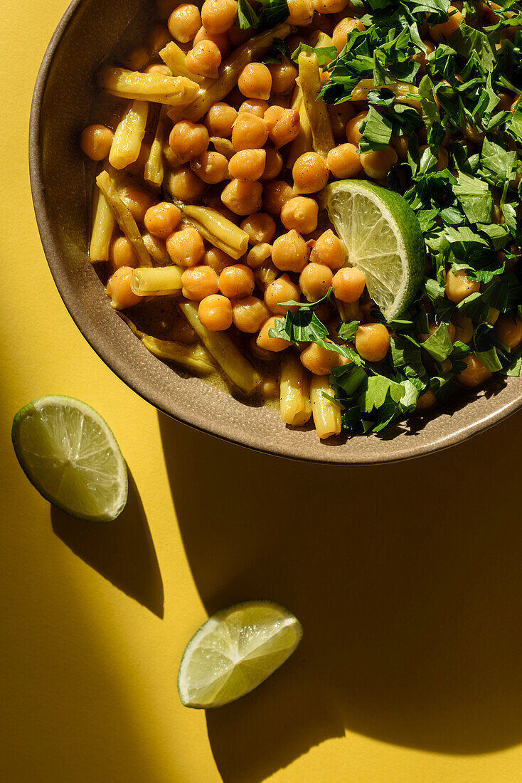 The dish of chickpeas and asparagus beans is seasoned with a slice of lime and chopped parsley. Top view.
