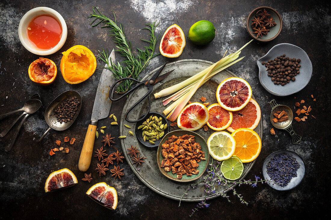 Flat lay Anordnung von bunten Zitrusscheiben, Fruchtsäfte, Zitronengras, Kräuter und Gewürze auf dunklem Hintergrund. Zutaten für hausgemachtes Tonic Water für Cocktails