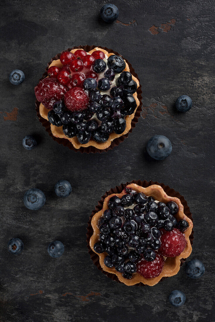 Pastry basket with blueberries and raspberries. Cake on a dark background. View from above