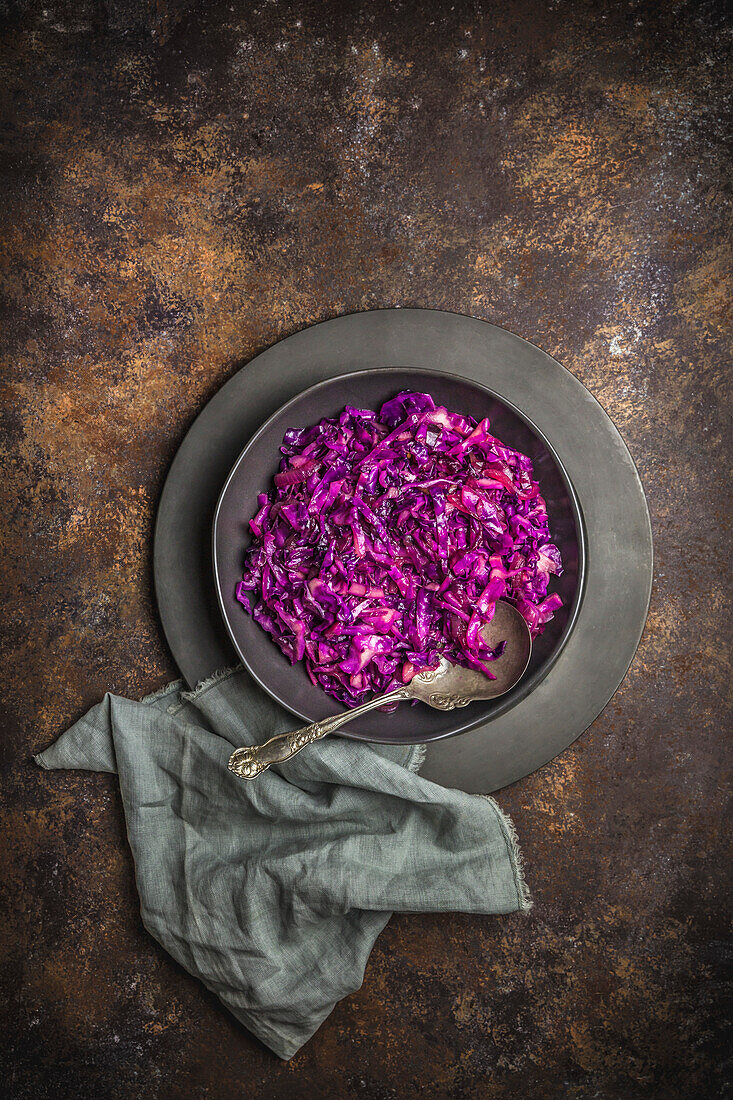 Overhead shot of braised red cabbage in a dark bowl on a rusty background