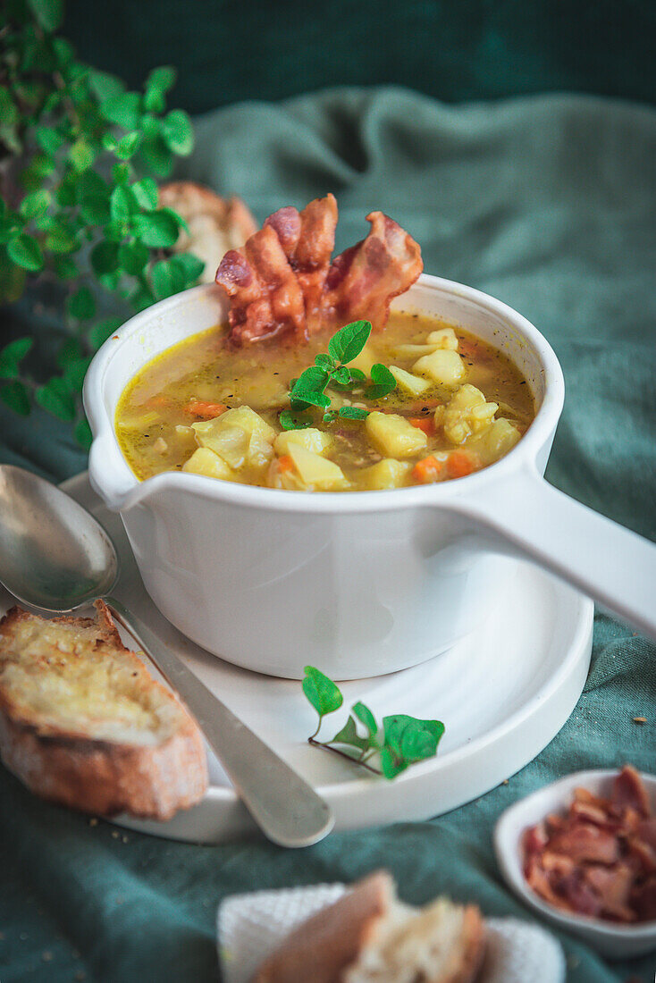 Potato and cabbage soup served with bacon strips in a white bowl