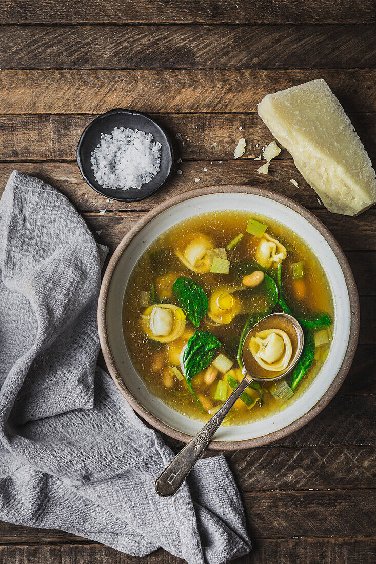 Tortellini, Spinat und Brühe in Schale mit Löffel, Parmesan und Serviette_weit