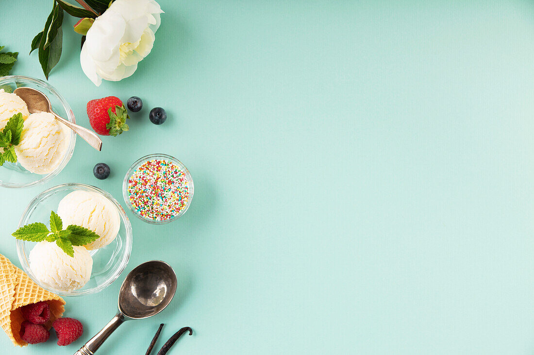 Vanillekugeln, Minzblätter in Glasschale, Streusel, Beeren und Blumen auf pastellfarbenem hellblauem Hintergrund, Ansicht von oben, Banner, Kopierbereich. Sommerliches Minimal-Konzept