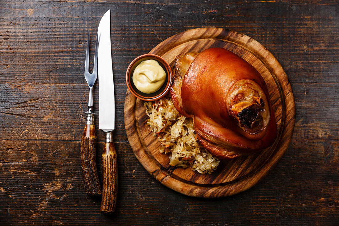 Roasted pork knuckle with braised cabbage and mustard on wooden board