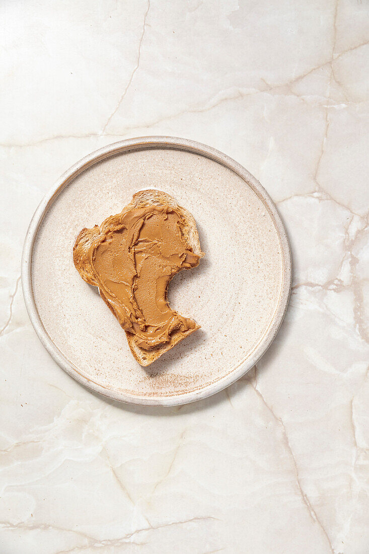 Peanut butter on toast, with bite mark on ceramic plate