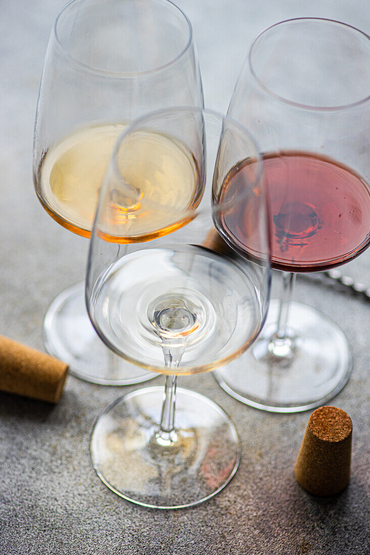 High angle of three main types of Georgian dry wines - white, red and amber - on a grey concrete table with a corkscrew and a cork