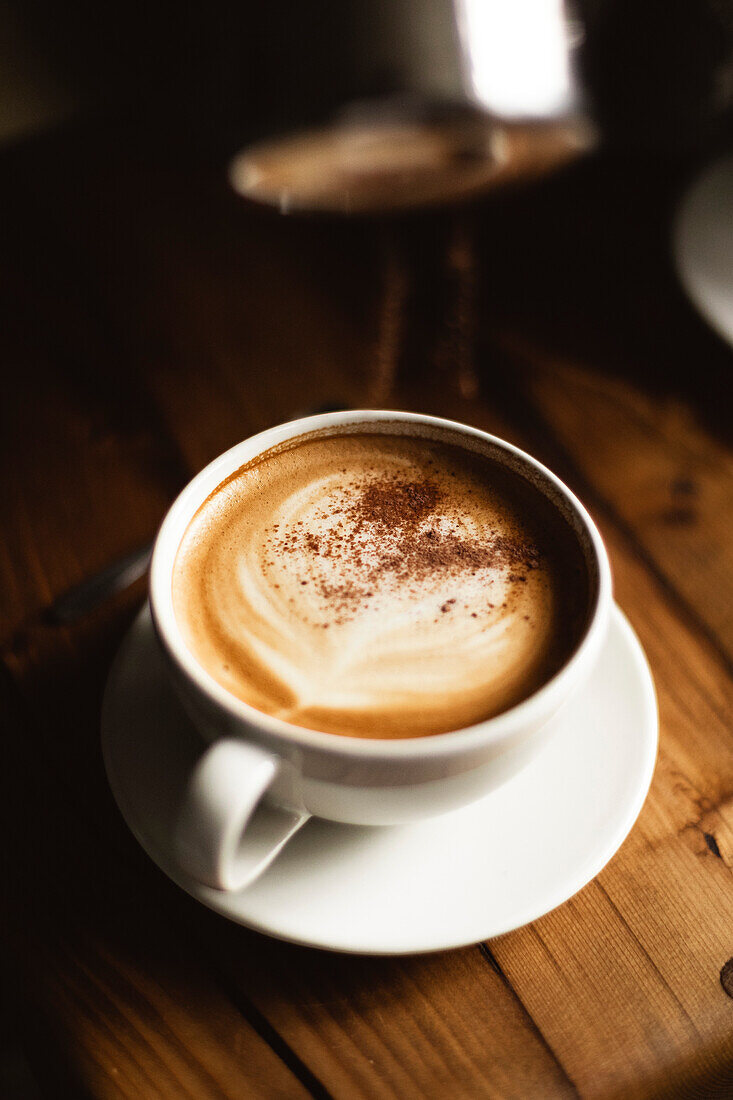 Kakaopulver auf Kaffee in weißer Tasse auf Holztisch gestreut