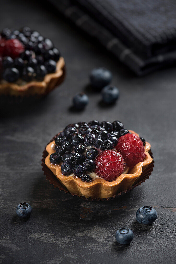 Pastry basket with blueberries and raspberries. Tart on a dark background