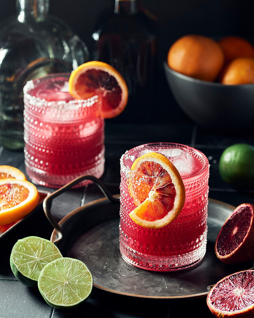 Zwei Gläser mit Blutorangen-Granatapfel-Margaritas auf dunklem Hintergrund