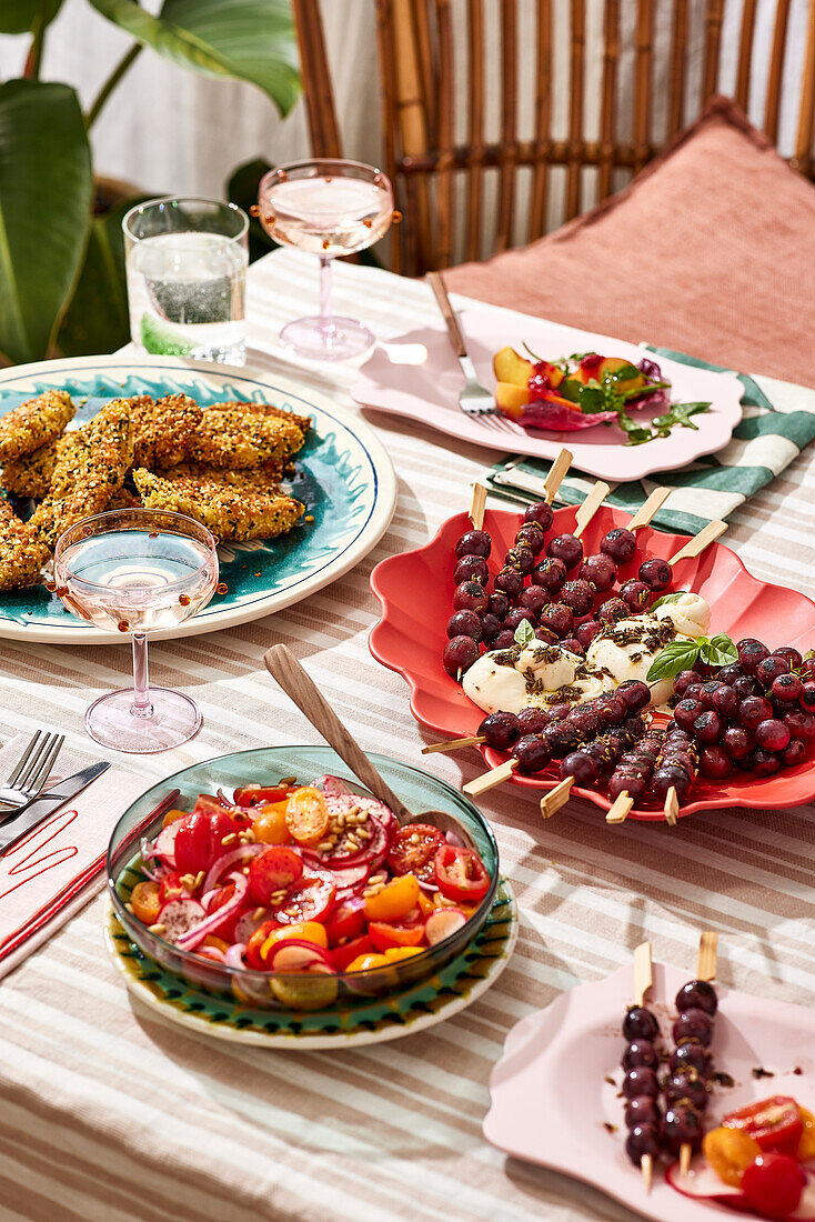 A picnic with salad at an outdoor table, with fresh fruit and fried food, on a striped tablecloth