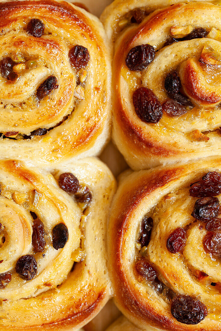 A close-up of four sweet rolls filled with lemon curd, sultanas and pistachios. They are unglazed