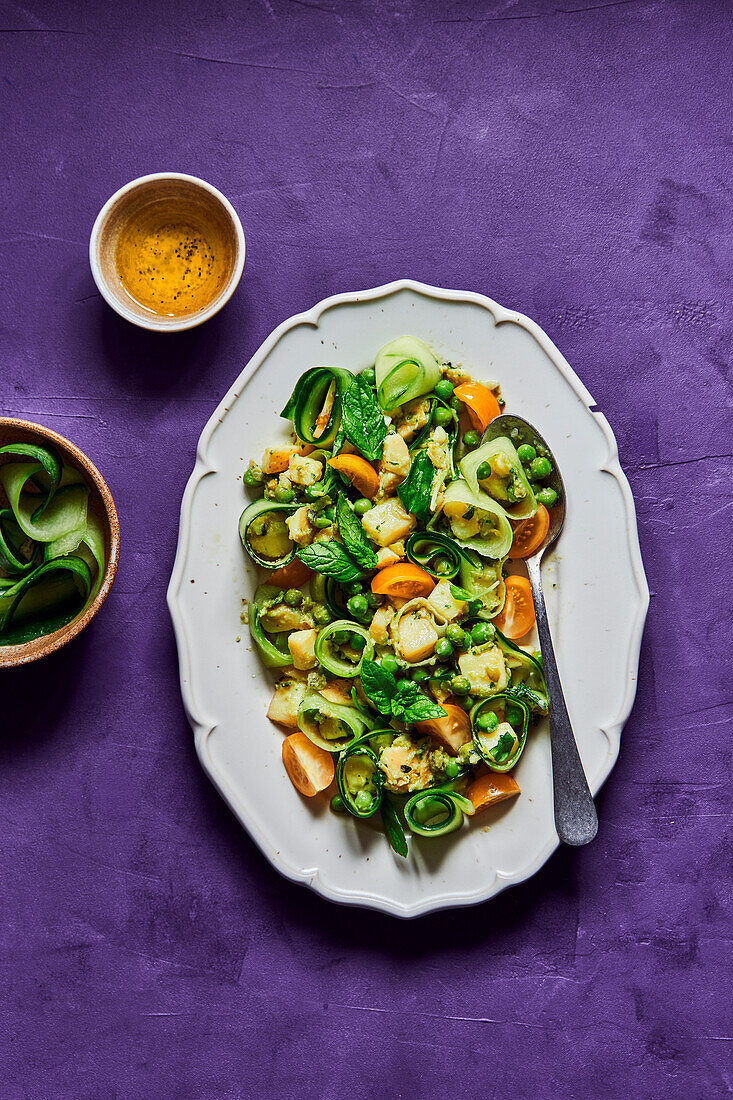 Green pea, cucumber, potato and tomato salad on a purple background with dressing