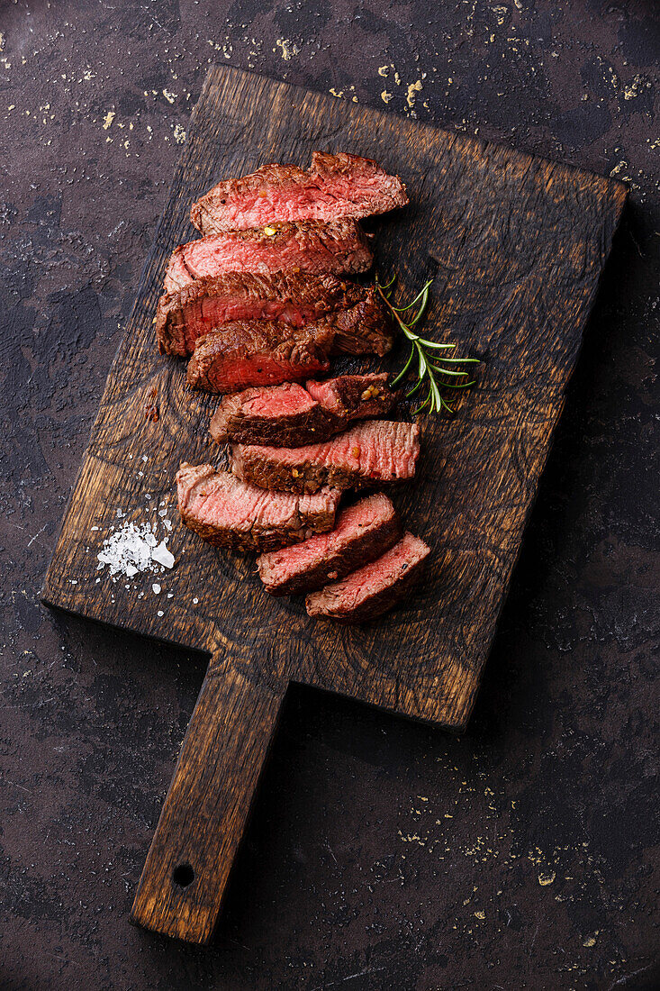 Sliced, medium grilled beef steak on a wooden cutting board