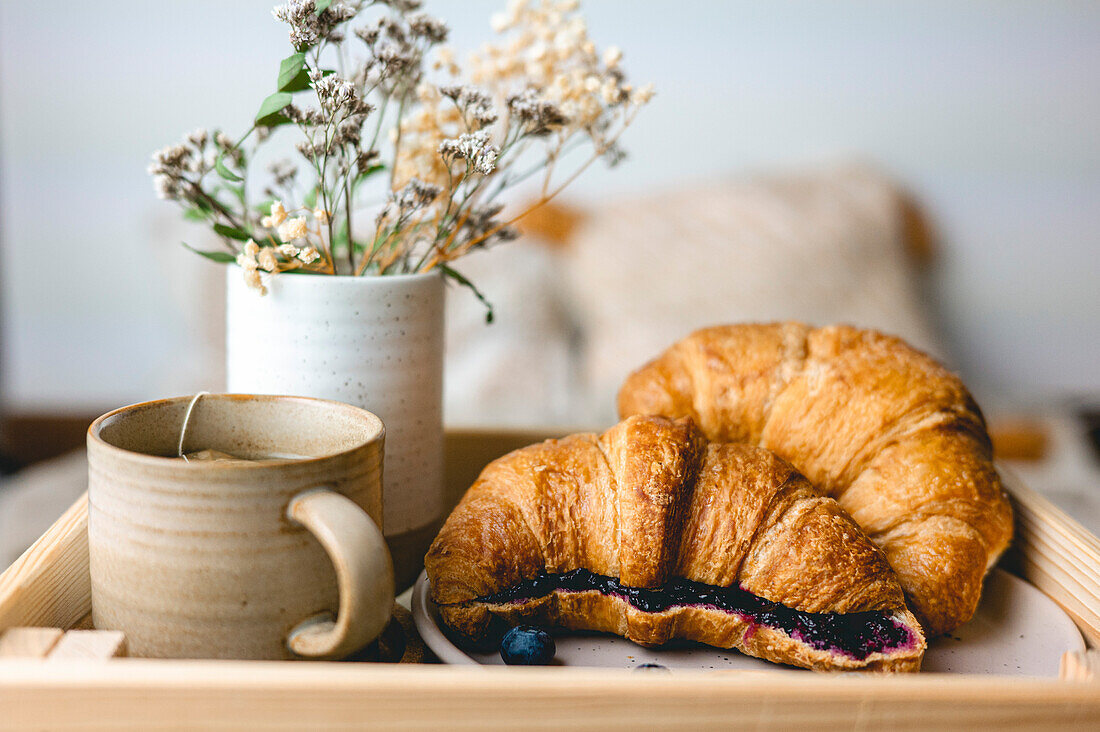 Frühstück im Bett mit frisch gebackenen Croissants mit Blaubeermarmelade und Tee in einem Becher