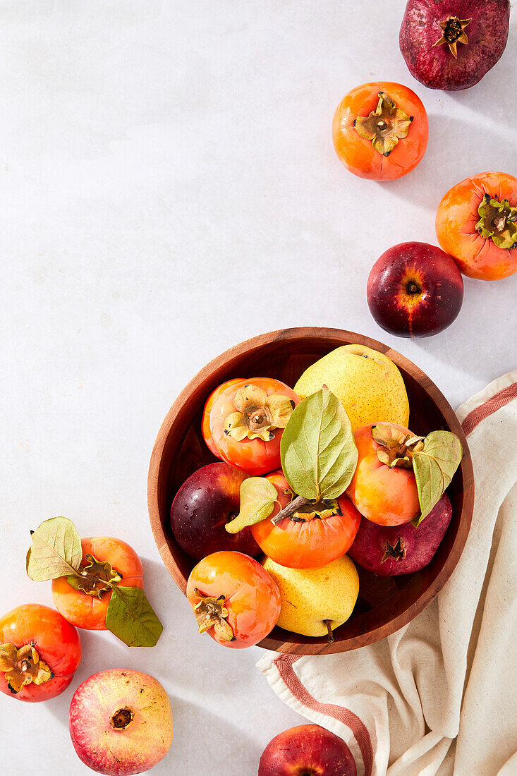 Pomegranates, persimmons, pears and apples in a bowl on a neutral background