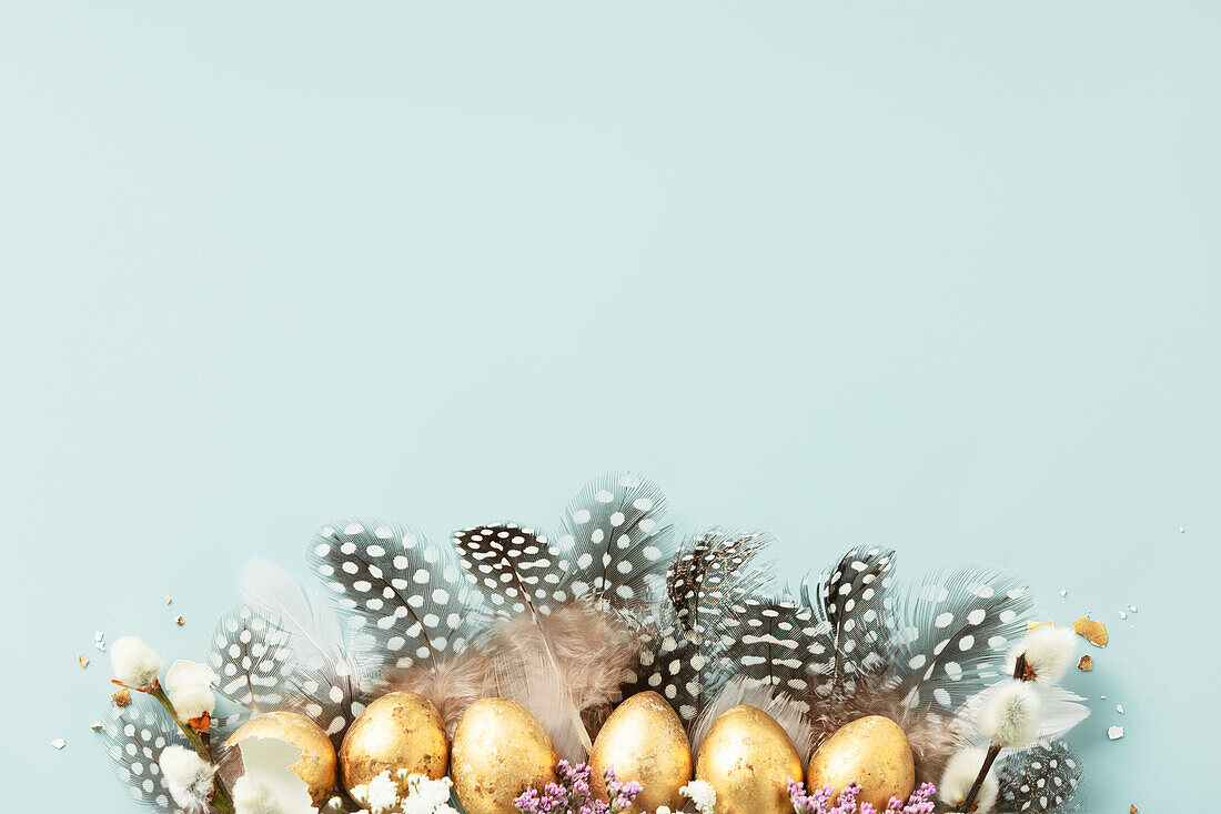 Raw of golden quail eggs and quail feathers on a blue background. Beautiful modern minimalist Easter composition. Copy space, top view, flat lay