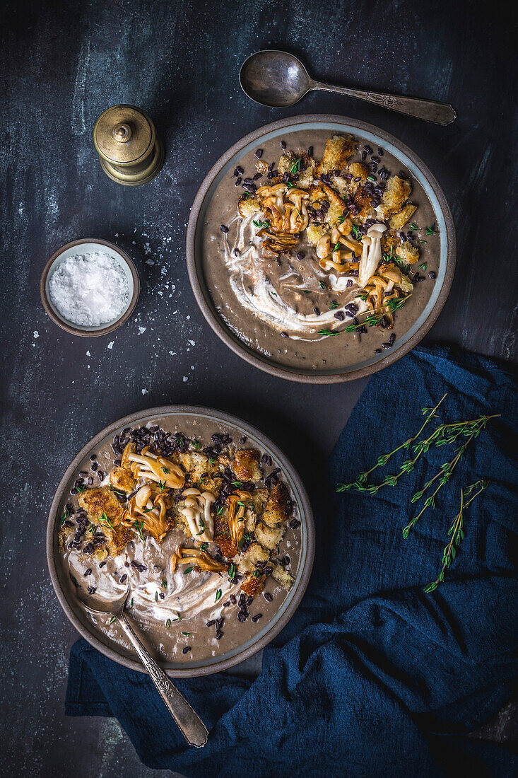 Two bowls of creamy mushroom soup with fried mussels and crouton garnish, overhead