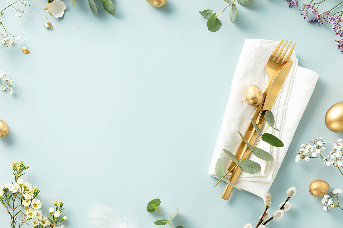 Easter table decoration. Stylish Easter brunch table with eggs, golden cutlery and spring branches laid flat on a blue background top view