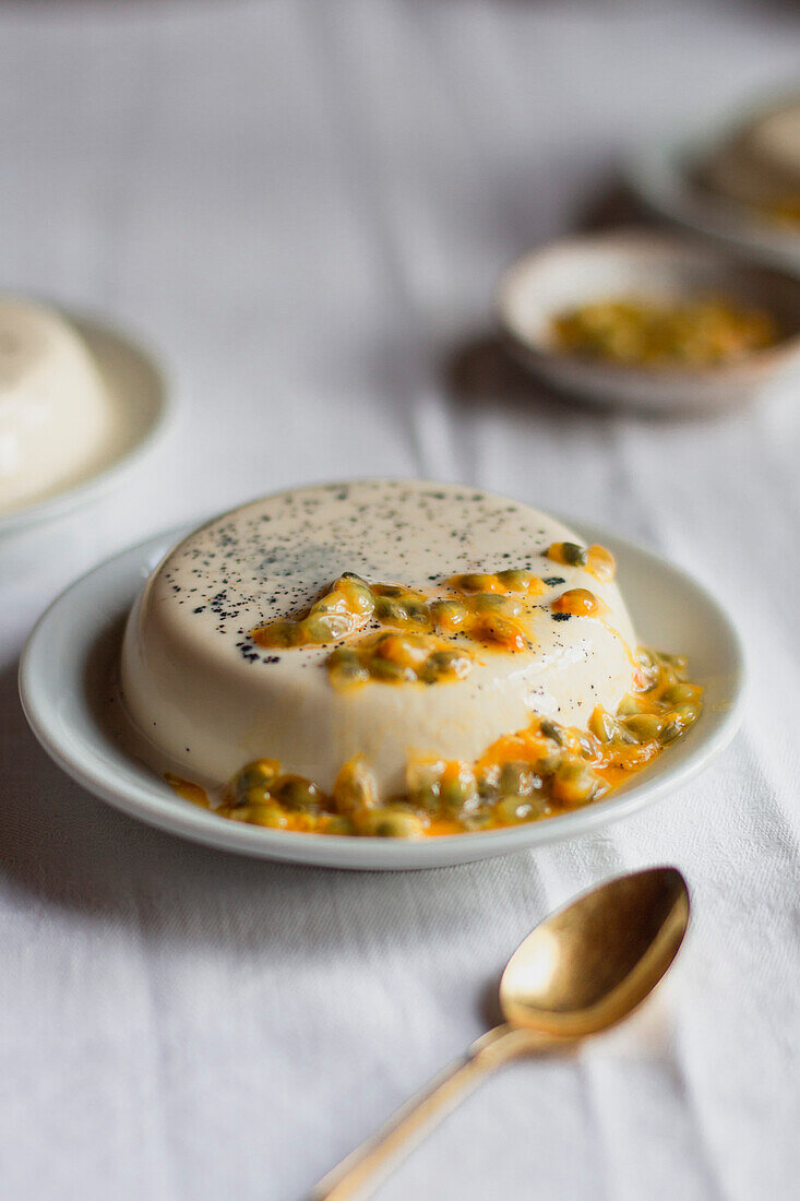 Passionsfrucht-Panna-Cotta mit goldenem Löffel auf weißem Tischtuch