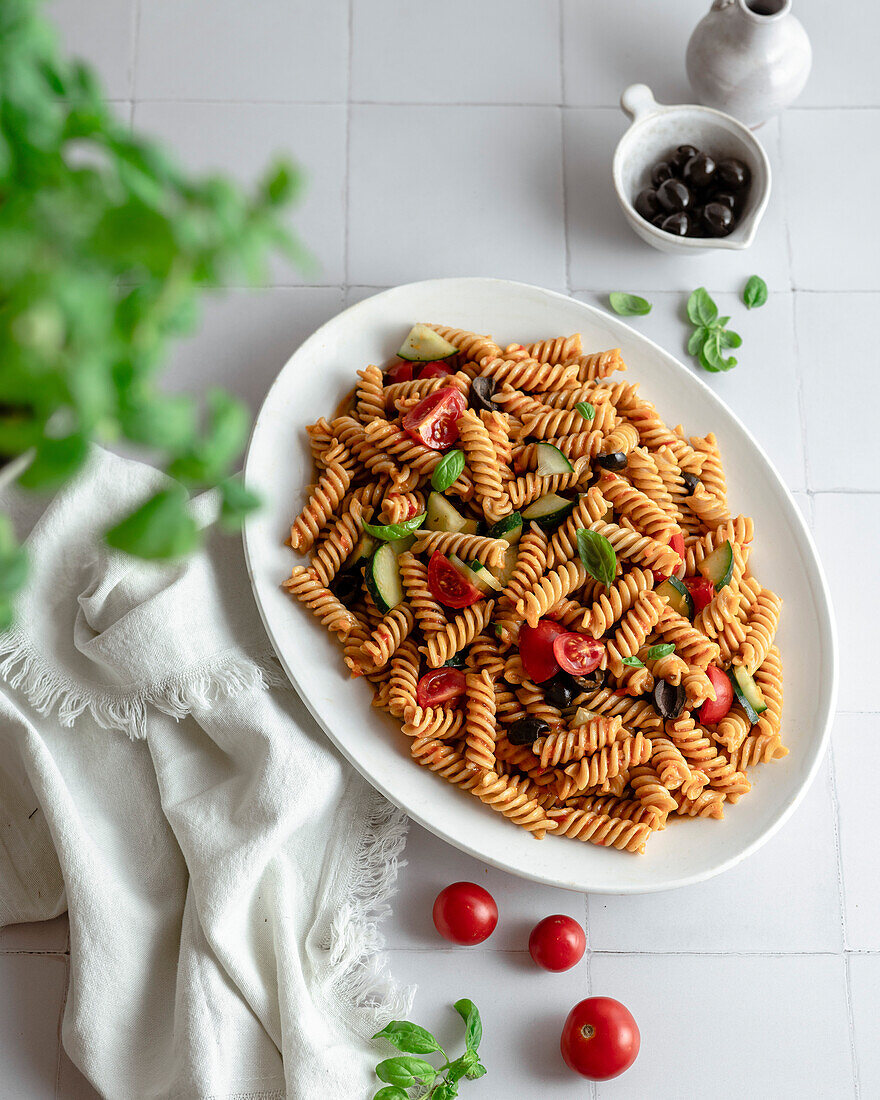 Mediterrane Nudelschale mit frischem Basilikum, Oliven, Kirschtomaten und Gurke