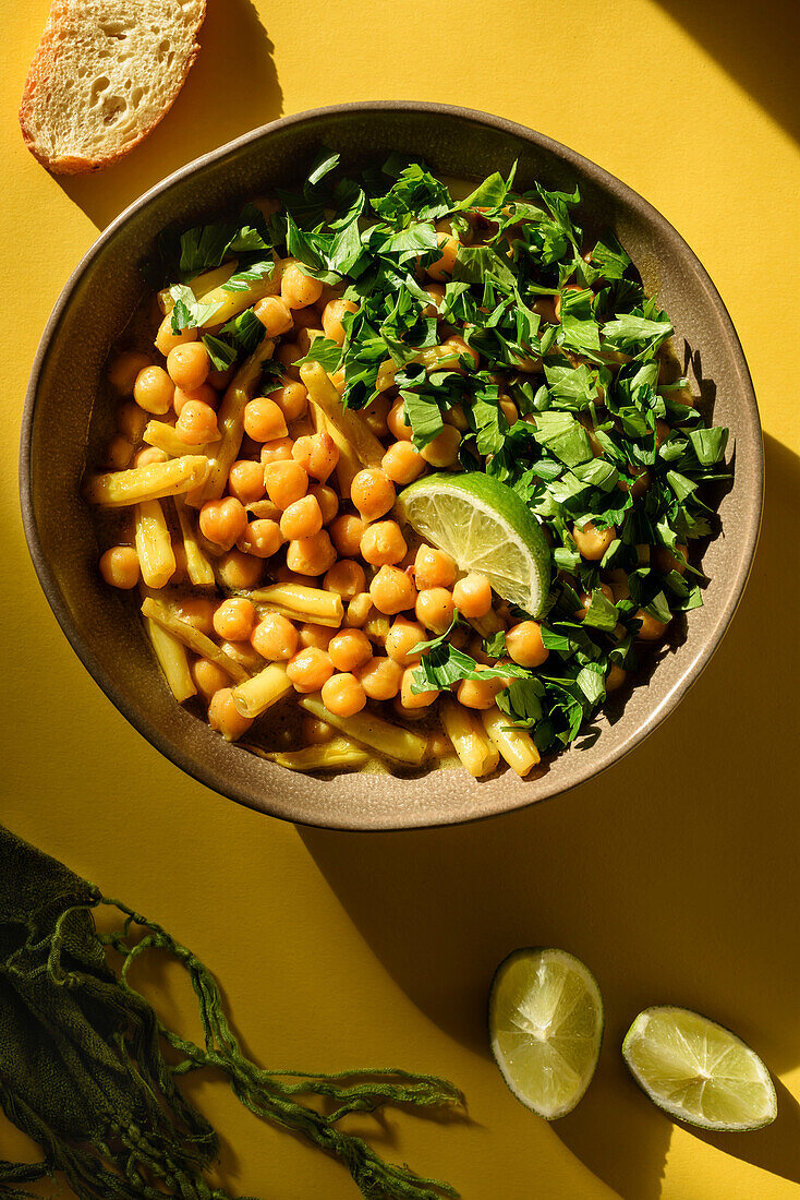 The dish of chickpeas and asparagus beans is seasoned with a slice of lime and chopped parsley. Top view.