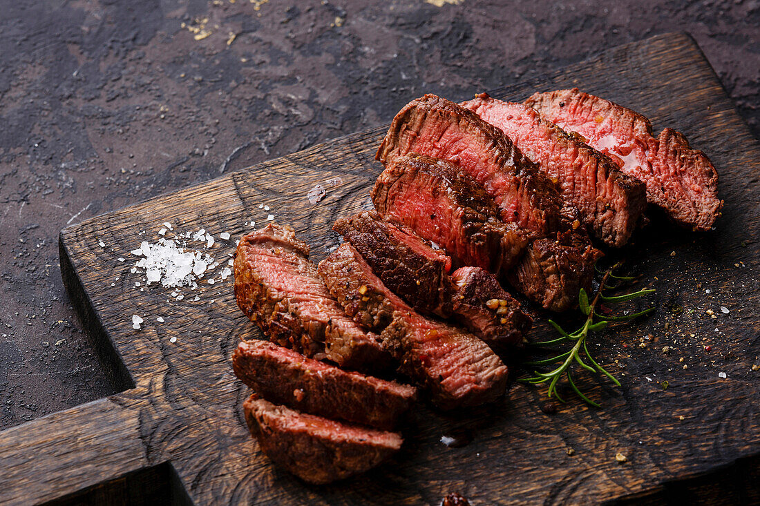 Sliced grilled steak with roast beef and rosemary on a wooden cutting board