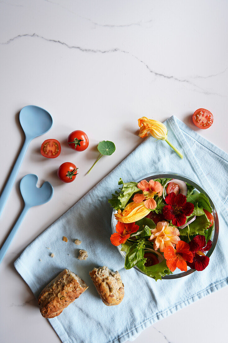 Mediterraner Salat mit Zucchini, Kapuzinerkresse und essbaren Rosenblüten auf weißem Marmorhintergrund mit negativem Kopierraum