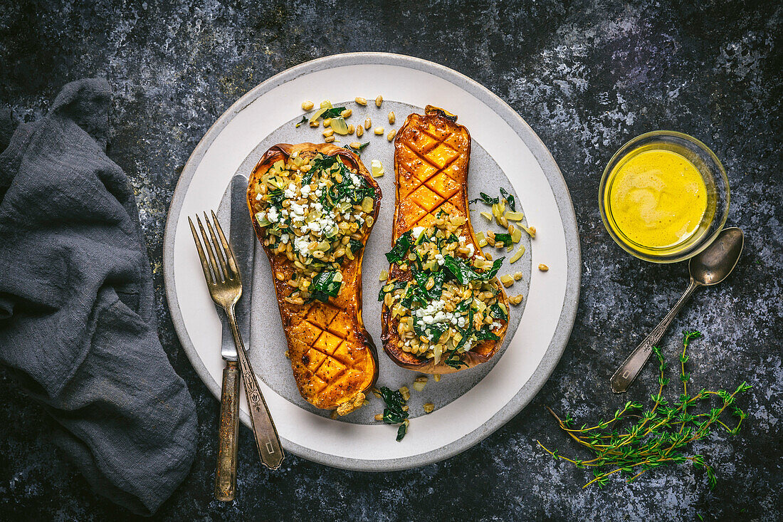 Mustard-glazed butternut squash halves filled with farro and kale on plate with glaze in bowl, from above