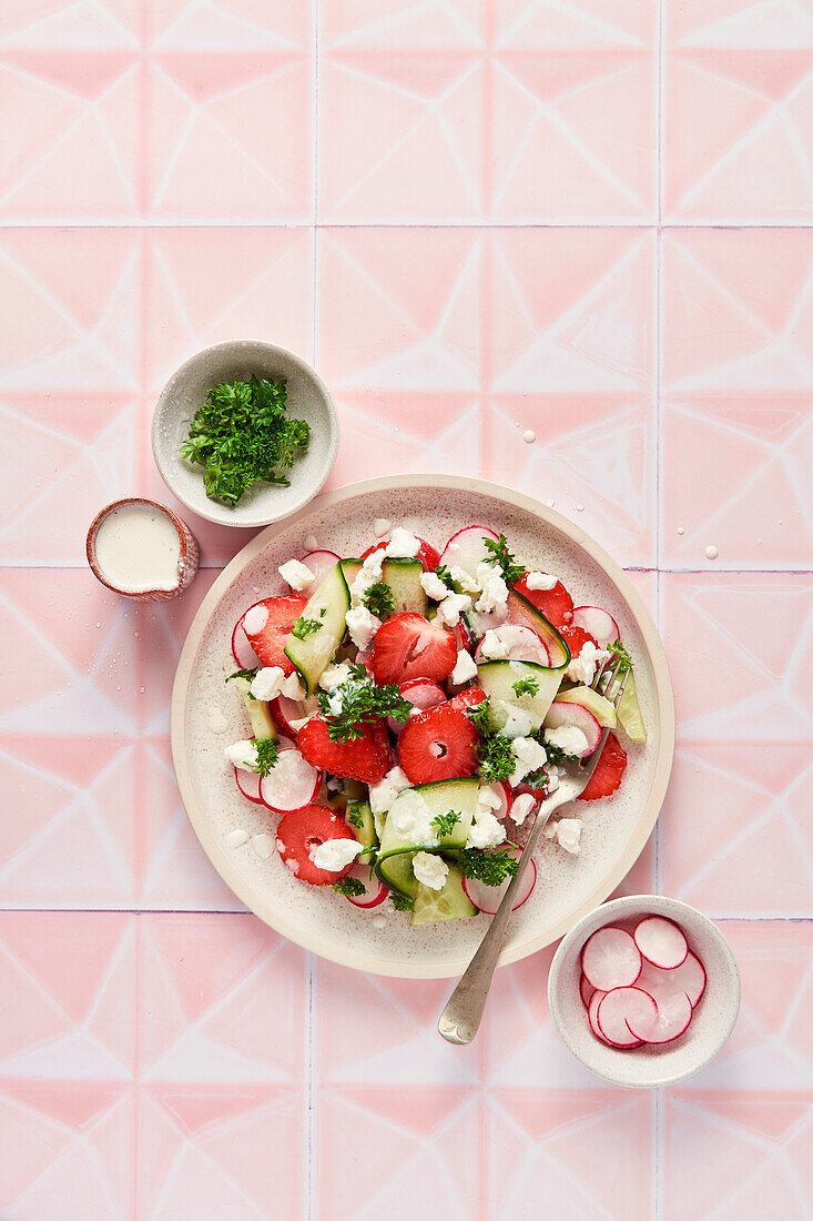 Frühlingssalat mit Erdbeeren, Gurken, Rettich und Petersilie auf rosa Kacheln