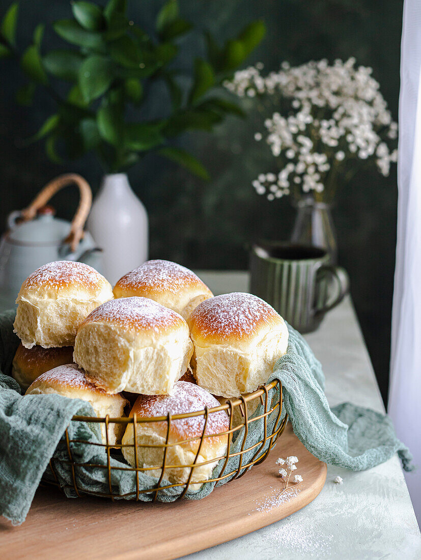 Homemade milk and cream cheese buns in a basket with a cloth next to a window